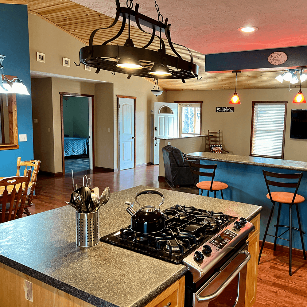 A modern kitchen featuring a stove, kettle, and bar seating with a view into an adjoining living area.